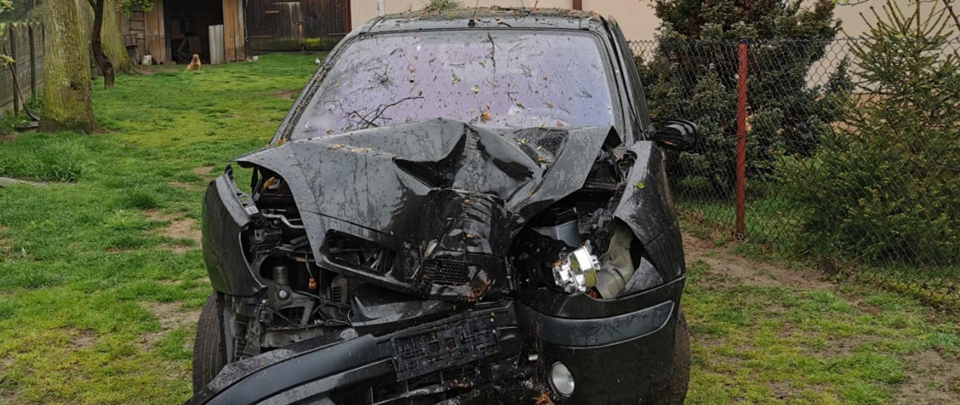 Miejsce zdarzenia widoczny uszkodzony samochód osobowy na posesji.