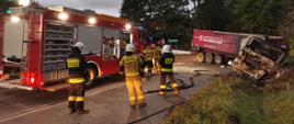 Samochód ciężarowy ze zniszczoną wskutek pożaru kabiną. Na pierwszym planie strażacy z rozwiniętymi liniami gaśniczymi