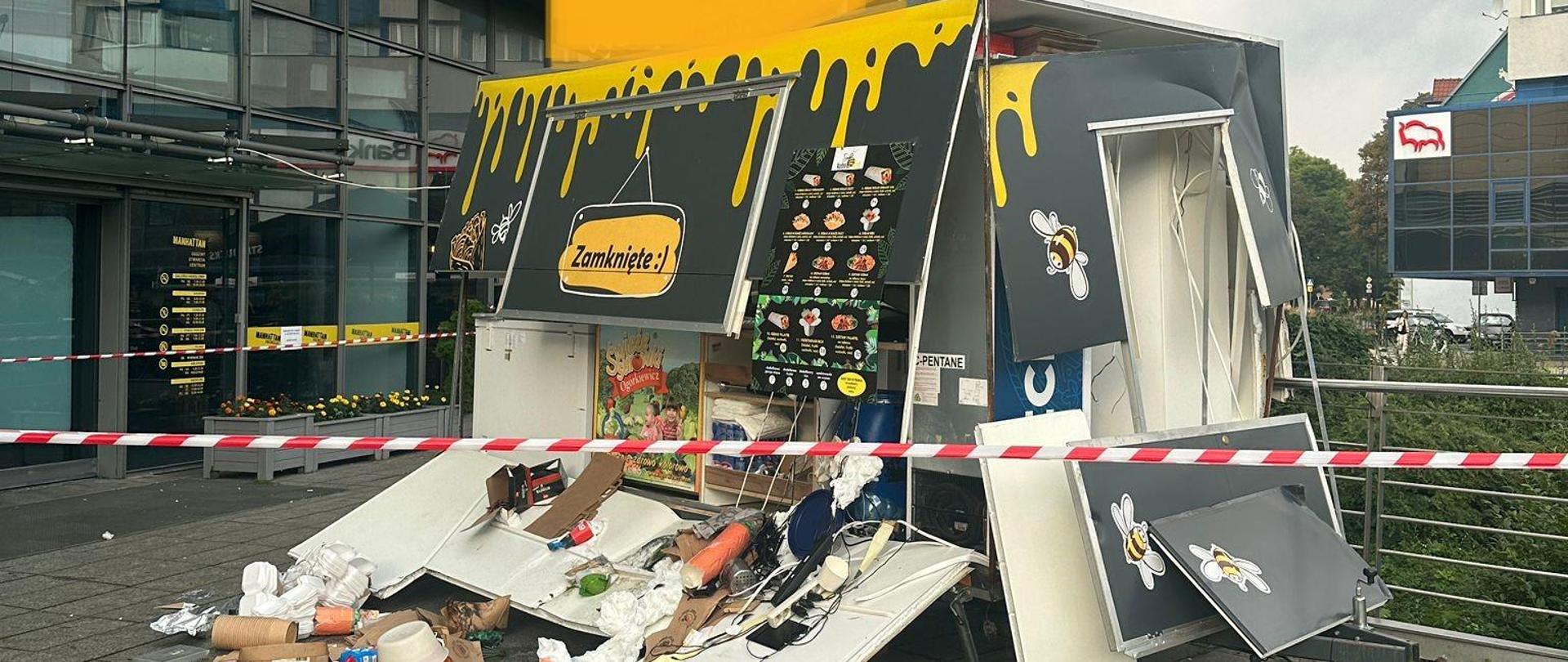 Przyczepa gastronomiczna uszkodzona po wybuchu. W tle centrum handlowe.