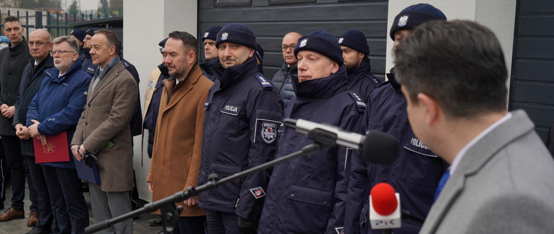 Grupa osób na otwarciu Posterunku, widoczni m.in. Wiceminister Tomasz Szymański i insp. Jakub Gorczyński (w centrum) oraz w lewym rogu Dyrektor WBZK Sławomir Szymański