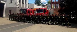 Strażacy uczestnicy kursu na tle czerwonych samochodów bojowych i budynki Komendy w Szamotułach