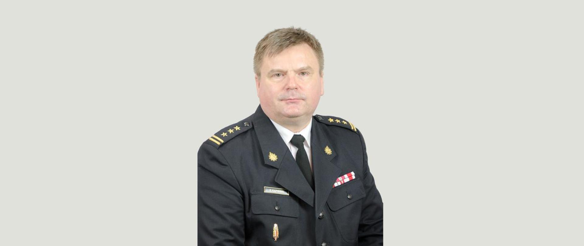 Komendant Powiatowy PSP st. bryg. mgr inż. Zbigniew Kąpiński w mundurze na szarym tle.
