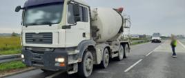Na pierwszym planie (od lewej): przód i lewy bok zatrzymanej do kontroli drogowej betoniarki przez patrol mazowieckiej ITD. W tle: za przeładowaną i niesprawną technicznie betoniarką stoi oznakowany furgon mazowieckiej ITD.