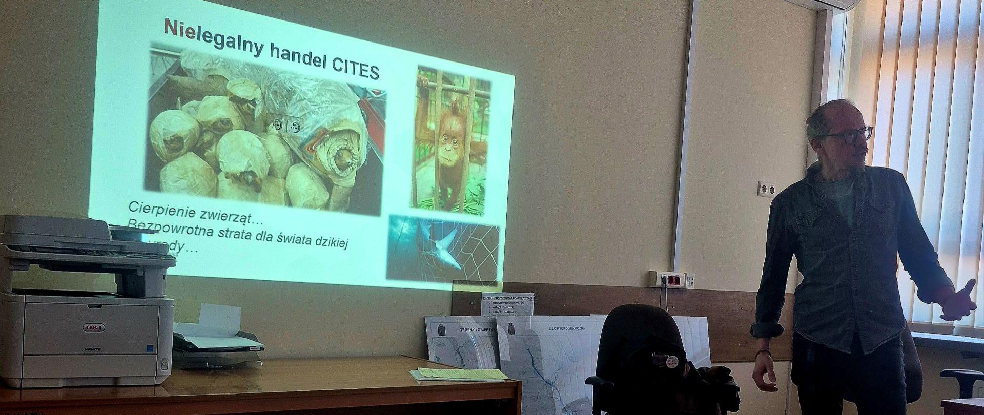 Prelegent prowadzi prezentację na temat nielegalnego handlu zwierzętami zagrożonymi (CITES). Na ekranie wyświetlone są zdjęcia przedstawiające przypadki przemytu oraz slajd opisujący konsekwencje dla świata dzikiej fauny.