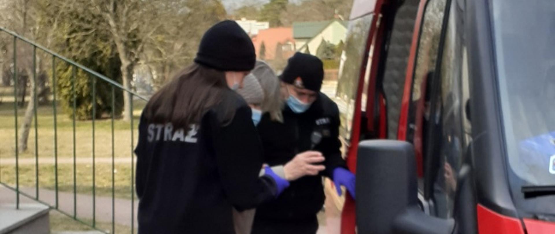 transport seniora na szczepienie, strażacy asekurują seniora podczas wchodzenia do samochodu strażackiego