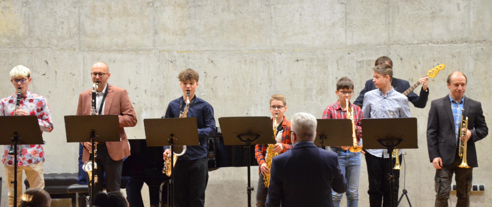 Mężczyżni i chłopcy grają na instrumentach dętych na scenie sali koncertowej