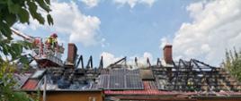 Pracujący strażacy w koszu wysięgnika usuwający skutki pożaru dachu budynku mieszkalnego