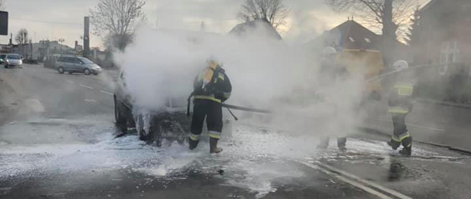 Droga, auto się dymi, strażacy w aparatach powietrznych gaszą.