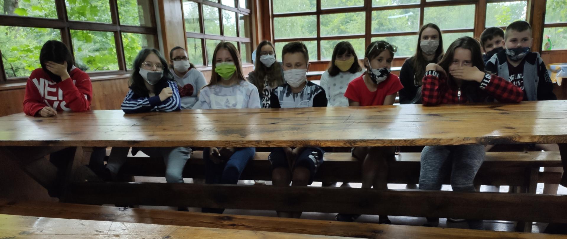 Grupa młodzieży, siedząca przy drewnianym stole podczas szkolenia z zakresu przestrzegania przepisów przeciwpożarowych i zasad bezpiecznego zachowania się podczas wystąpienia sytuacji kryzysowej