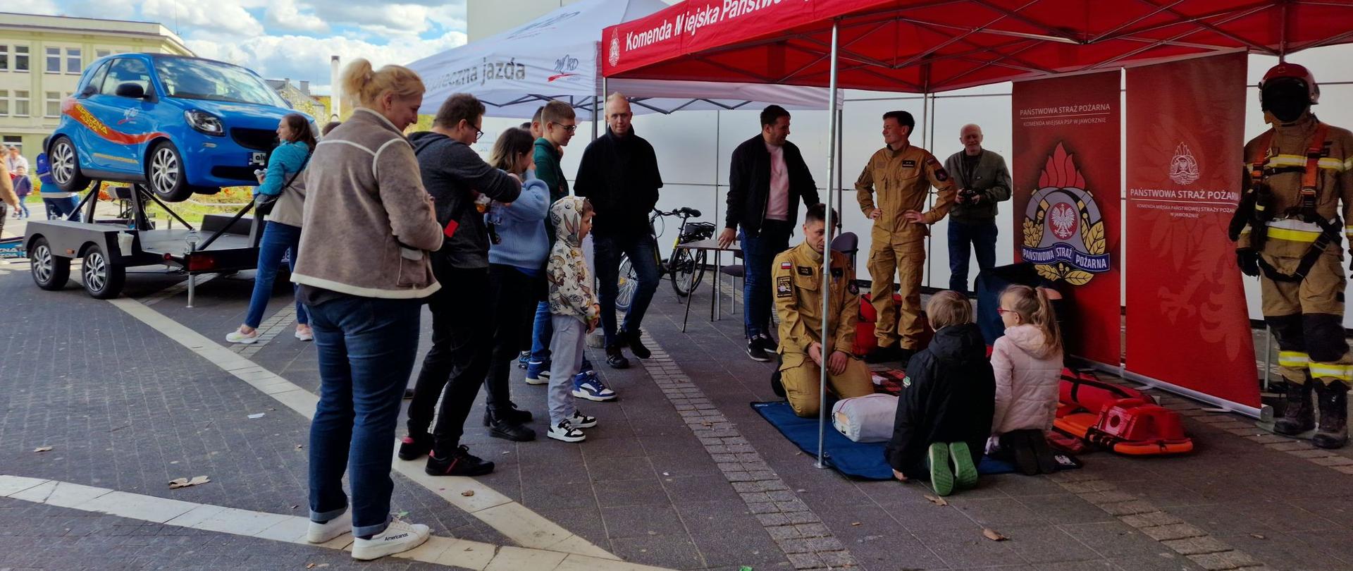 zdjęcie przedstawia namiot edukacyjny Komendy Miejskiej Państwowej Straży Pożarnej w Jaworznie zorganizowany w czasie Pikniku, w którym funkcjonariusze przedstawiają postępowanie podczas udzielania kwalifikowanej pierwszej pomocy.