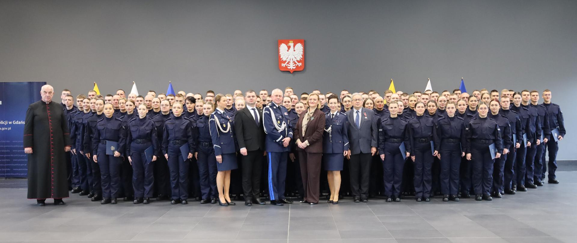 grupa osób większość w policyjnych mundurach pozuje do zdjęcia, w tle godło Polski