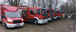 Samochody strażackie ustawione w punkcie przyjęcia sił i środków. Strażacy grupują się do zbiórki 