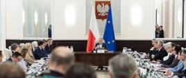 Posiedzenie Rady Ministrów - przyjęcie projektu ustawy budżetowej na 2026 r. Na centralnym miejscu Premier Donald Tusk, po bokach ministrowie. W tle flagi Polski i UE.