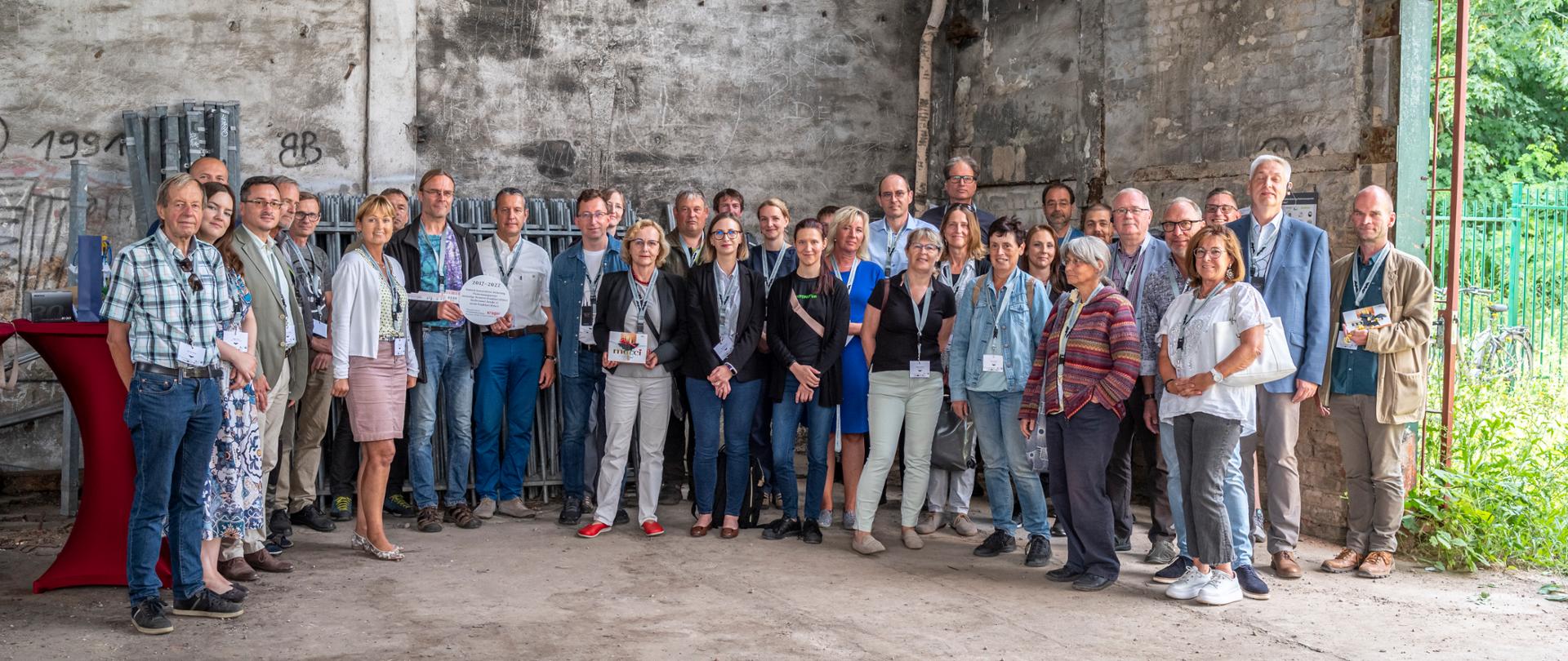 We wnętrzu starego budynku stoi grupa kilkudziesięciu osób, kobiet i mężczyzn pozujących do zdjęcia.