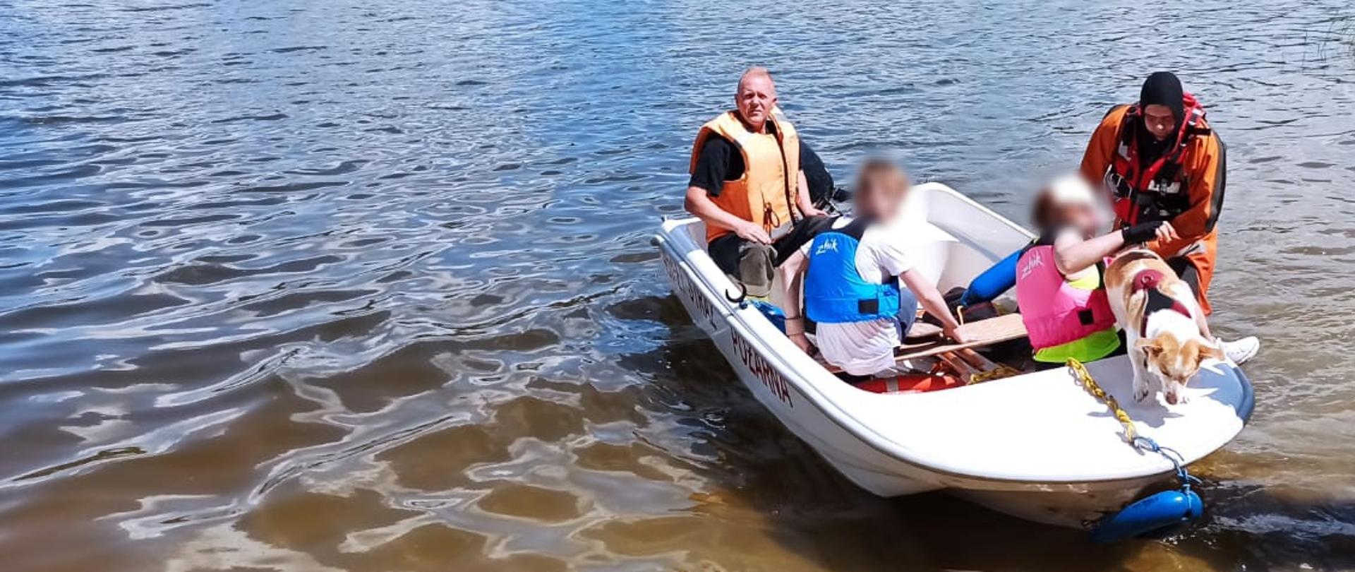 Zdjęcie przedstawia osoby ewakuowane z przewróconej żaglówki na brzeg przez strażaków z wykorzystaniem łodzi z silnikiem zaburtowym