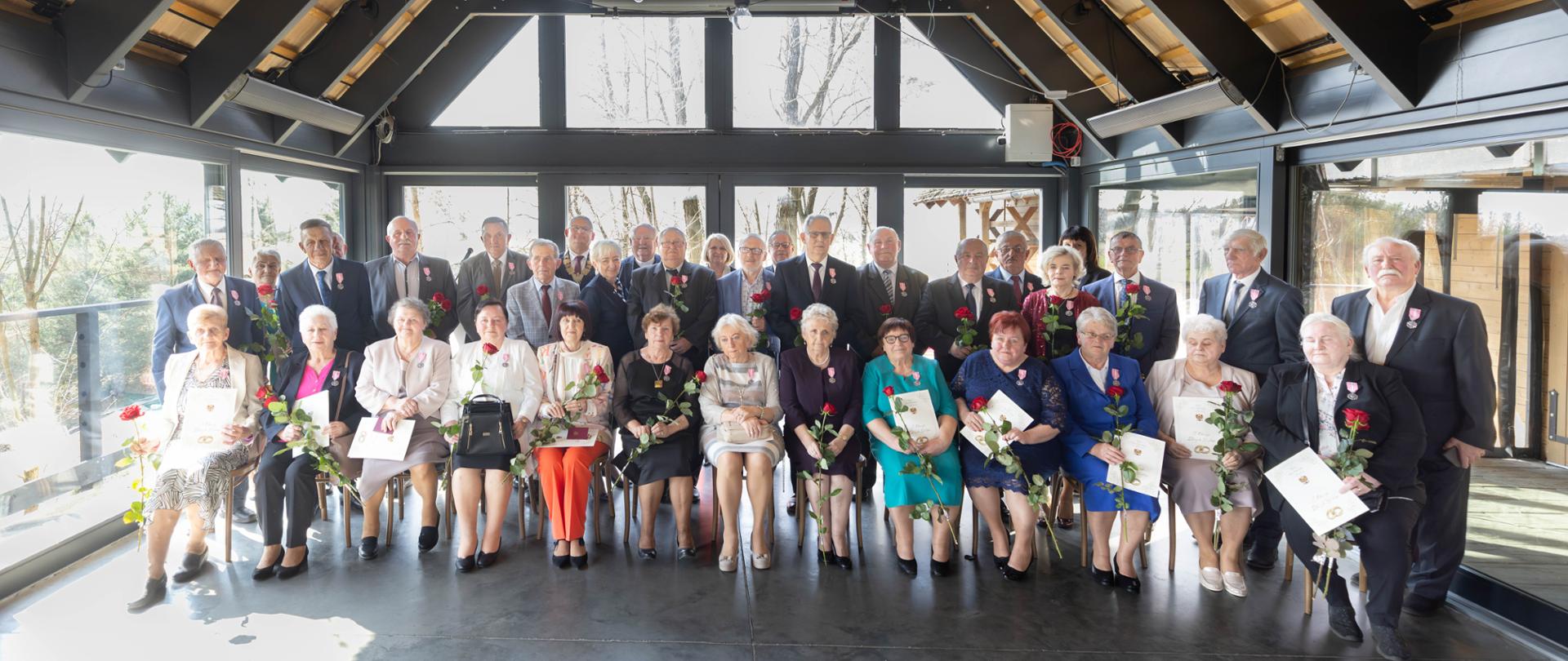 Pamiątkowa fotografia wojewody łódzkiego Doroty Ryl oraz zaproszonych gości z uhonorowanymi małżeństwami 