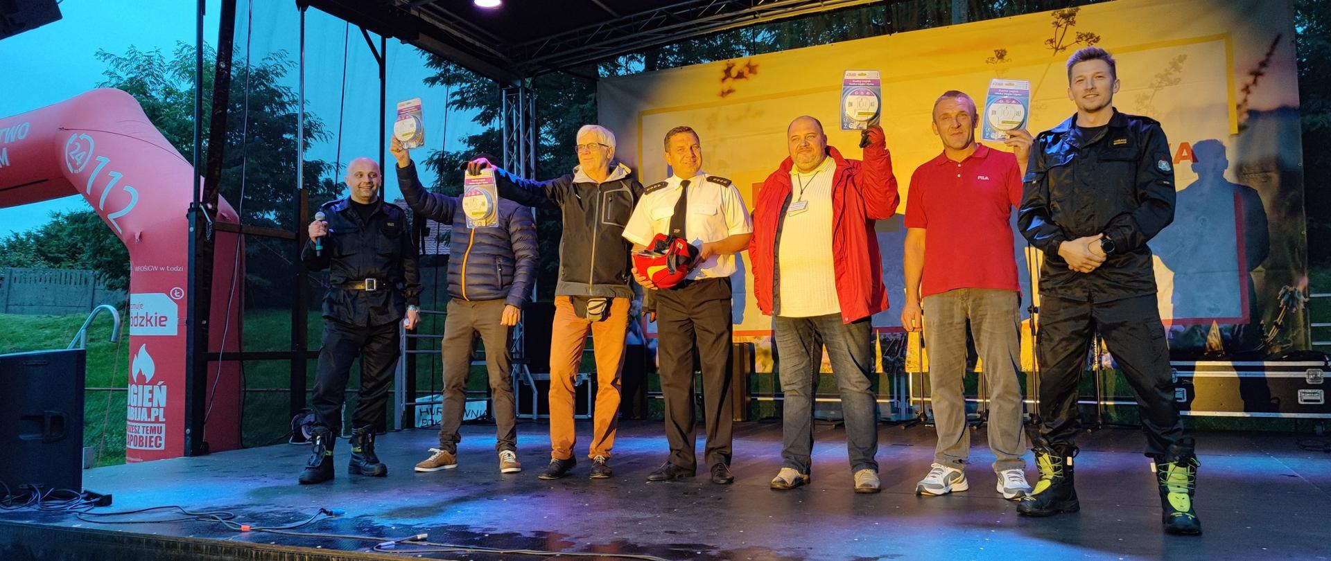 Zdjęcie przedstawia laureatów losowania czujek dymu i tlenku węgla. Obok widoczny zastępca dowódcy Jednostki Ratowniczo Gaśniczej oraz kapitan Tomasz Mendak, którzy wręczali nagrody.