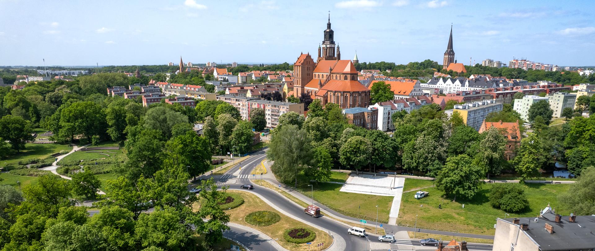 Widok z lotu ptaka na miasto, błękitne niebo, widoczne drzewa i wieże kościołów