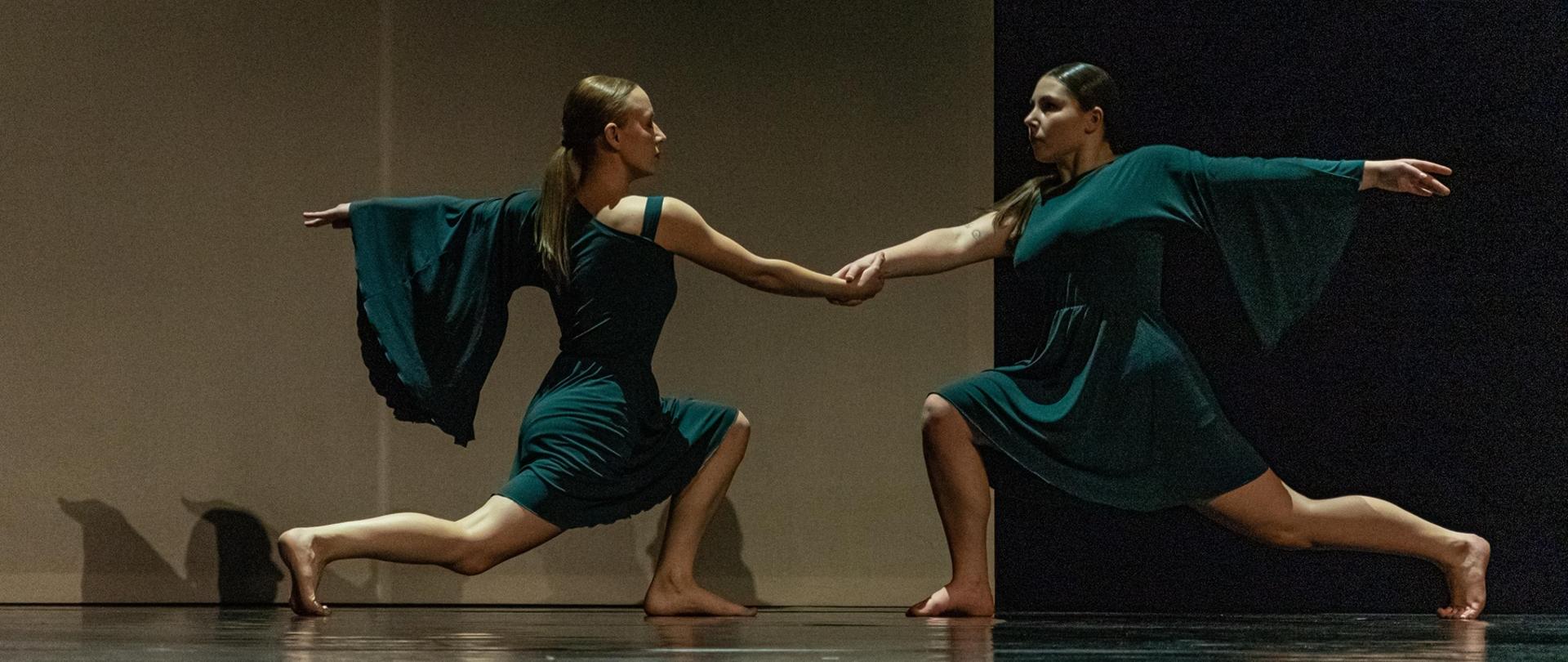 Na zdjęciu są dwie słuchaczki Studium w tanecznych pozycjach, skierowane twarzami do siebie w uklęku. Ubrane są w zielone sukienki. 