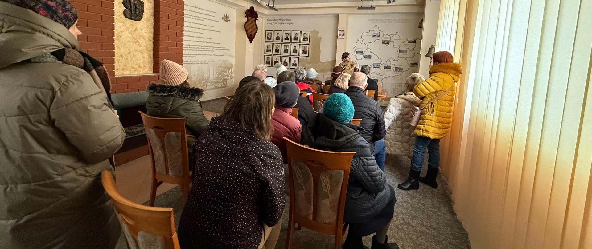 Fotografia przedstawia funkcjonariusza podczas prelekcji o bezpieczeństwie pożarowym. Przed nim siedzą słuchacze.