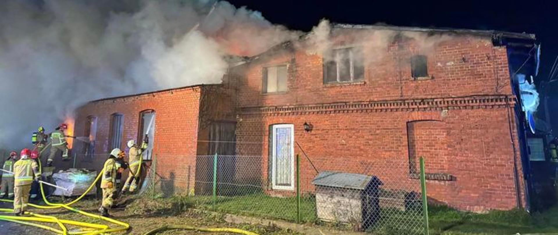 Strażacy w trakcie działań przy objętym pożarem budynku.