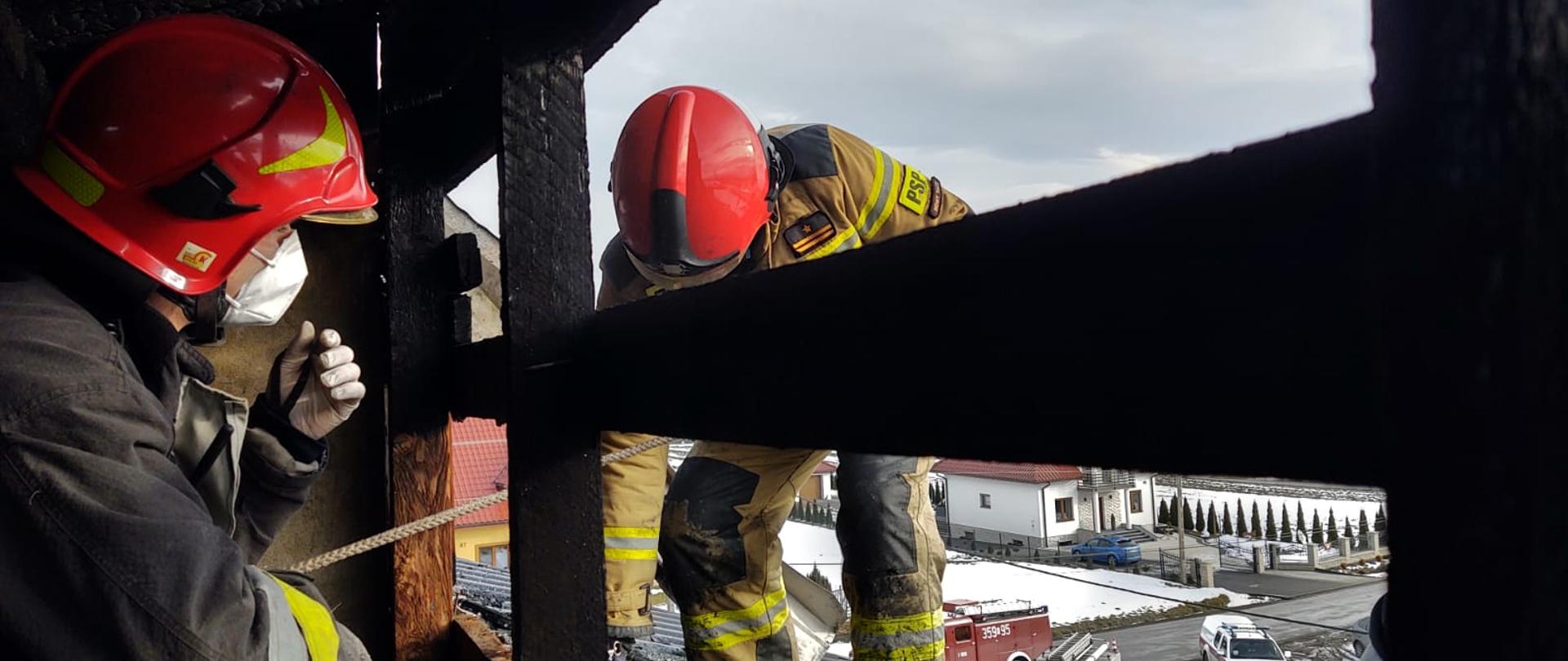 Dwóch strażaków prowadzi działania ratownicze na dachu i poddaszu.