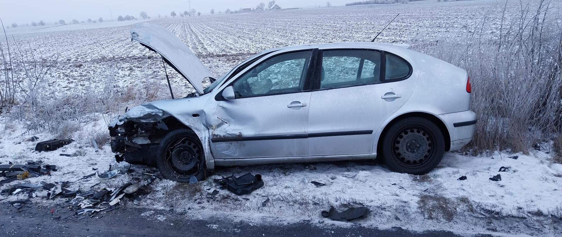 Srebrny samochód z uszkodzonym przodem na poboczu drogi