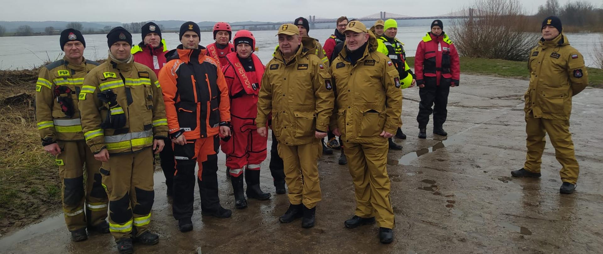 Grupa strażaków na skraju zbiornika wodnego, spoglądająca w lewa stronę