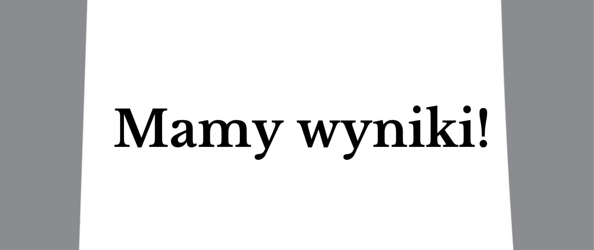 Grafika posiada szare tło, na którym znajduje się biała karteczka z czerwona pinezką. Na środku karteczki, jest napis "Mamy wyniki! ".