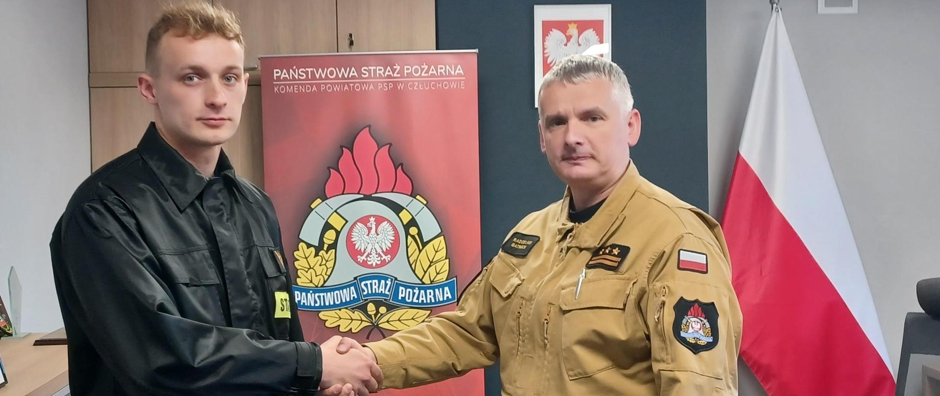 Komendant Powiatowy Państwowej Straży Pożarnej w Człuchowie st. bryg. Radosław Batruch stoi w gabinecie i wręcza akt mianowania na stanowisko dowódcy zastępu mł. asp. Zbigniewowi Wolter.