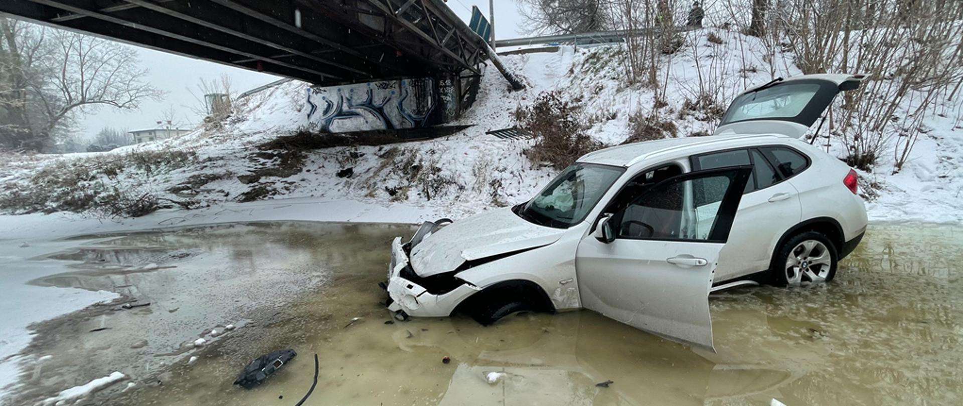 Samochód osobowy koloru białego stojący w zamrożonej rzece. 