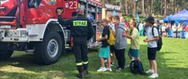 strażak przy samochodzie strażackim na trawie. obok uczniowie oglądający samochód