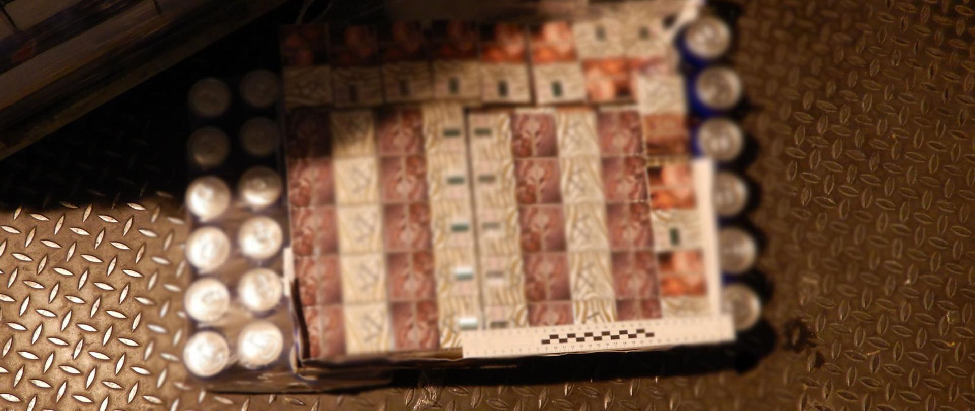 Na podłodze paczki z nielegalnymi papierosami wśród puszek z napojami gazowanymi