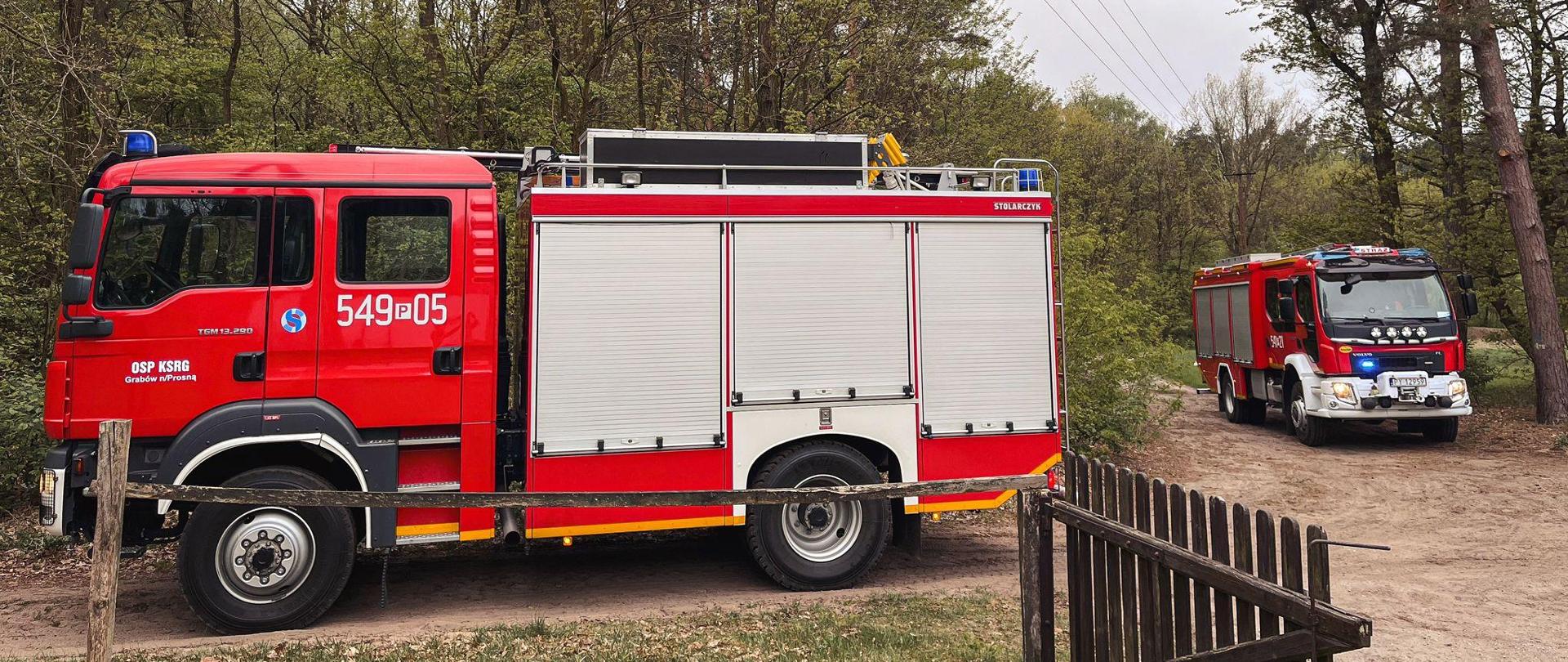Samochody gaśnicze stoją na drodze dojazdowej do miejsca zdarzenia. Na dalszym planie widać las.