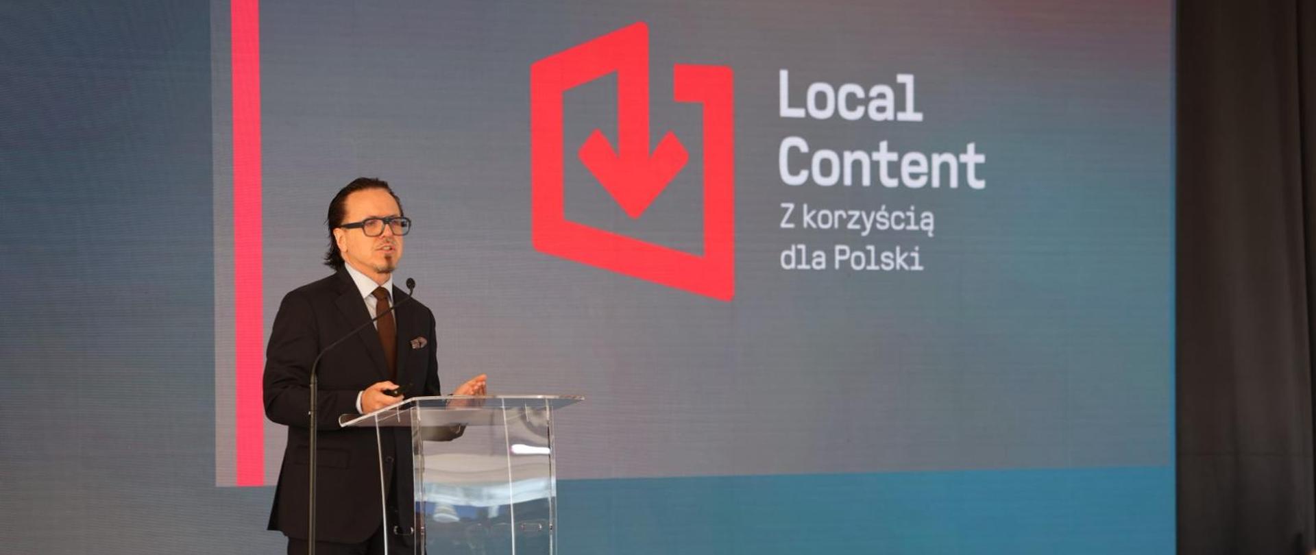 Minister Wojciech Balczun podczas inauguracji projektu "Local Content. Z korzyścią dla Polski, stoi za mównicą. W tle logotyp "Local Content. Z korzyścią dla Polski." 