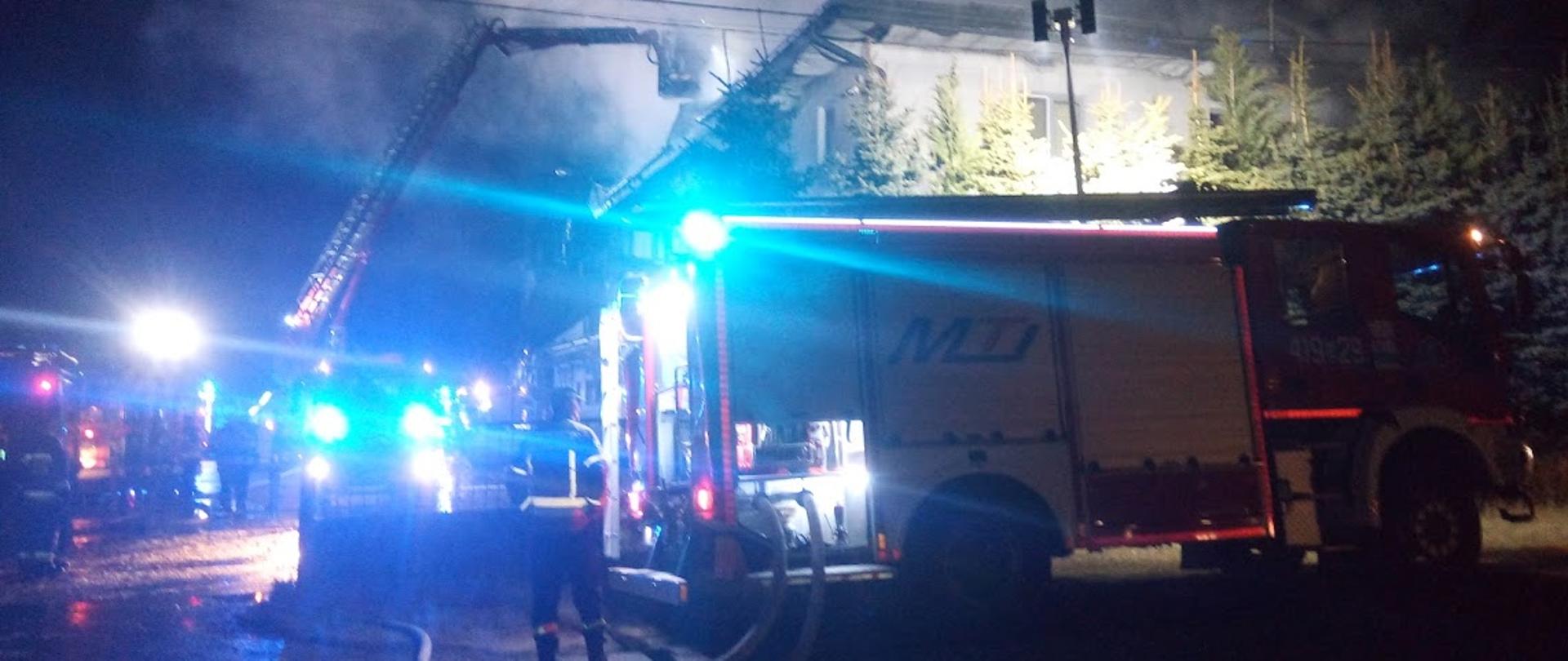 Zdjęcie przedstawia wozy ratowniczo-gaśnicze z włączonymi niebieskimi światłami ostrzegawczymi 