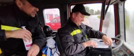 Dwóch strażaków OSP w kabinie pojazdu pożarniczego.