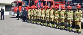 Pomorski komendant wojewódzki Państwowej Straży Pożarnej przemawia obok stoją strażacy za nimi samochody gaśnicze. 