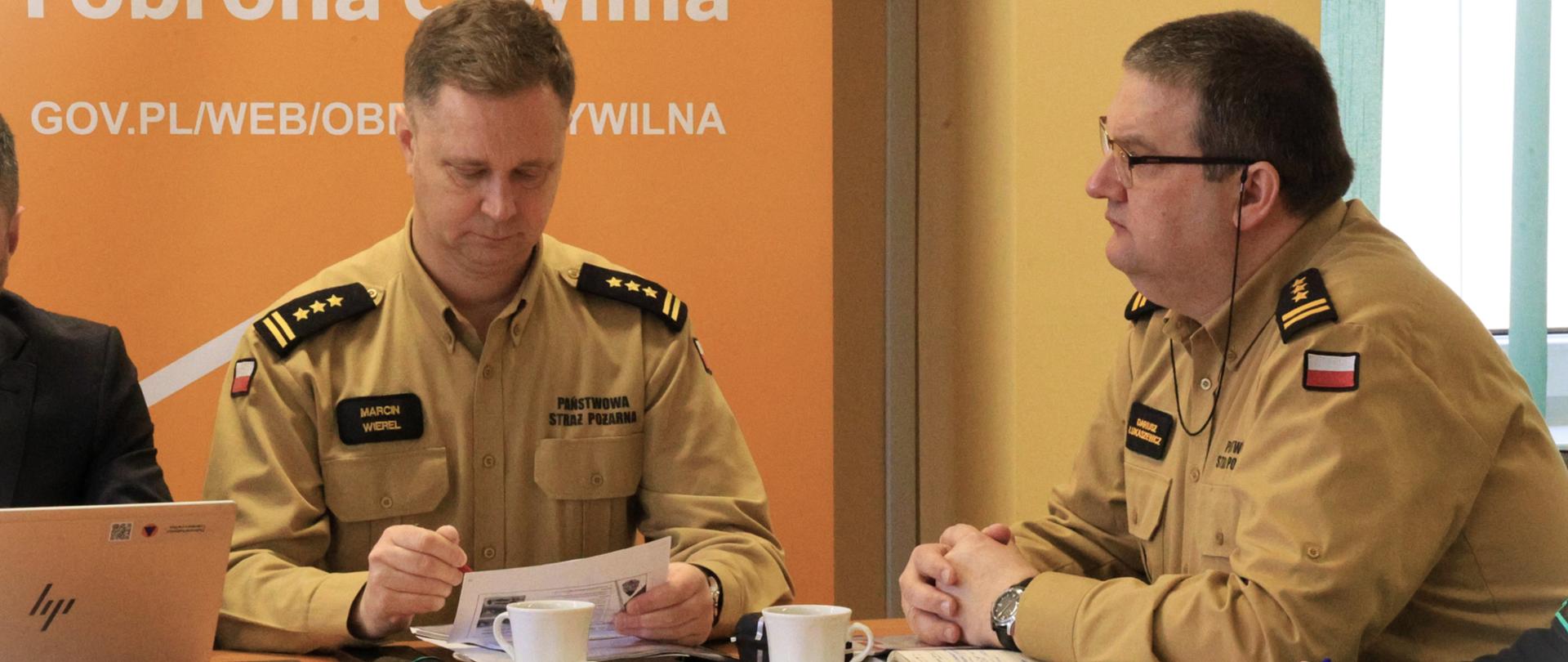 Suwalska konferencja dot. realizacji Programu Ochrony Ludności i Obrony Cywilnej na lata 2025-2026 - st. bryg. Marcin Wierel i st. bryg. Dariusz Łukaszewicz siedzą przy stole w trakcie spotkania