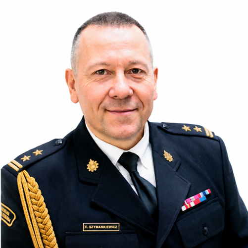 Portret Komendanta Powiatowego w mundurze strażackim na białym tle. Ma krótkie, siwe włosy i delikatny uśmiech. Na mundurze widoczne są pagony oraz odznaczenia