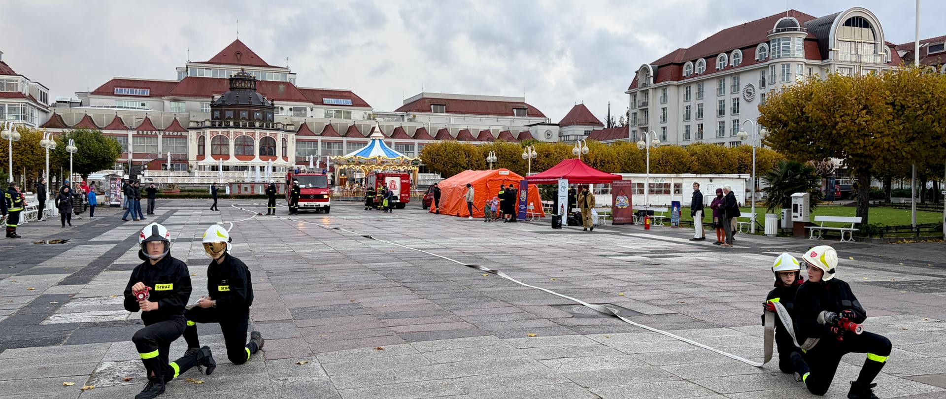Zdjęcie przedstawia strażaków podczas ćwiczeń trzymających węże pożarnicze na Placu Zdrojowym w Sopocie