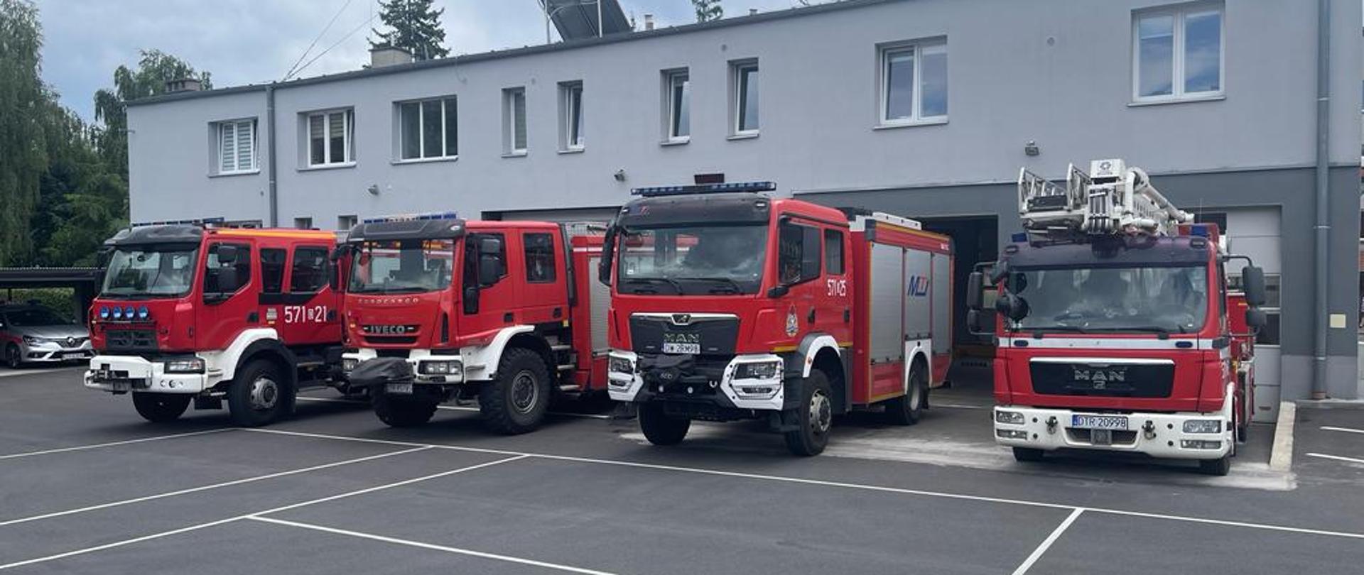 Ustawione obok siebie samochody bojowe. W tle budynek garażowy