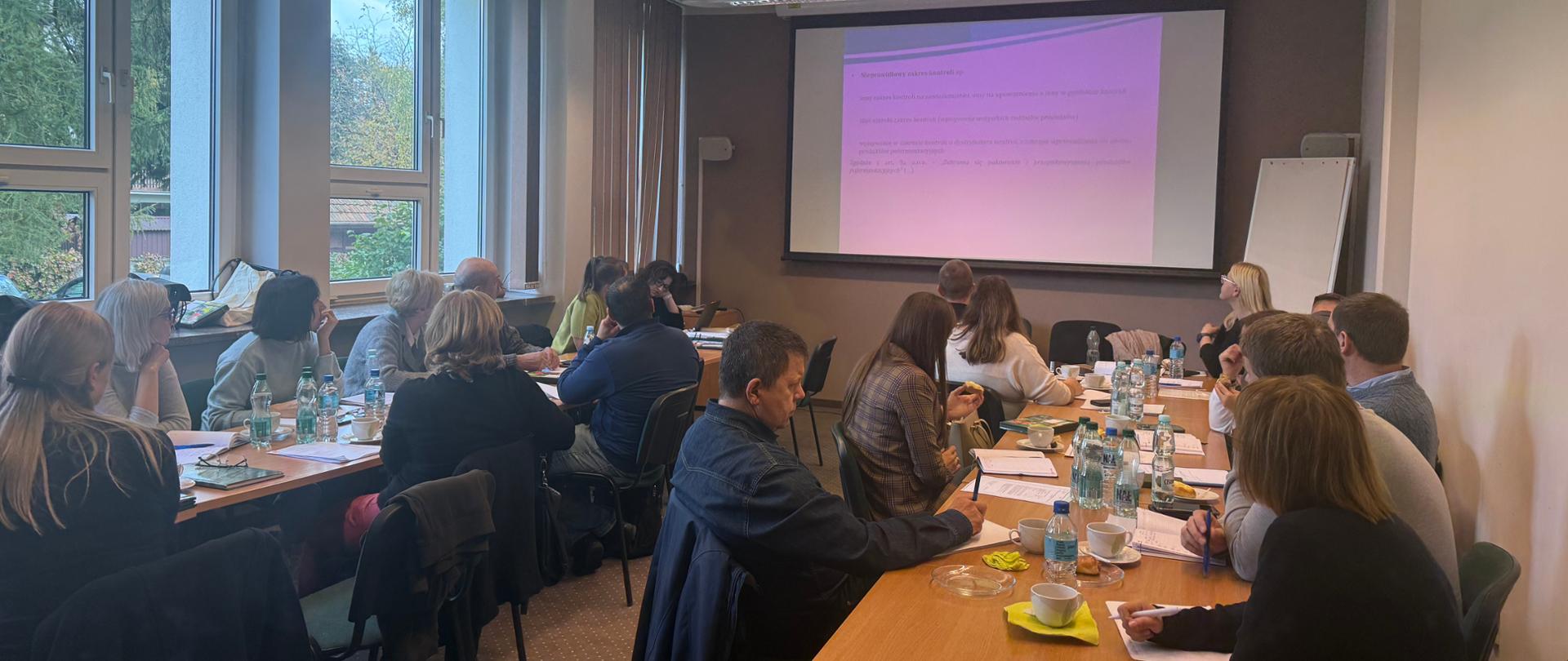 Grupa osób siedząca przy stołach na sali szkoleniowej