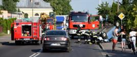 Zdjęcie przedstawia dwa wozy strażackie, trzech strażaków oraz samochód po dachowaniu