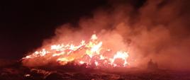 Zdjęcie w porze nocnej. Widać palący się stóg słomy.