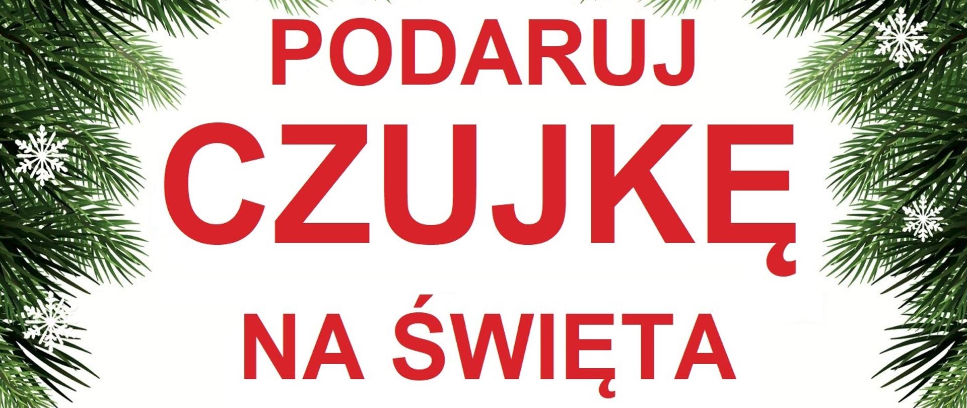 Plakat obramowany gałązkami świerku z napisem: "Podaruj czujkę na Święta", pod którym znajduje się czujka przepasana wstążką a pod nią napis " prezent który może uratować życie. Na dole logo PSP z opisem Komenda Powiatowa Państwowej Straży Pożarnej w Kartuzach.