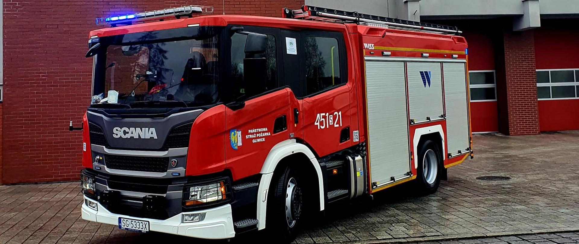 Czerwony samochód ciężarowy pożarniczy na tle Jednostki Ratowniczo Gaśniczej w Gliwicach Scania źródło KM PSP Gliwice