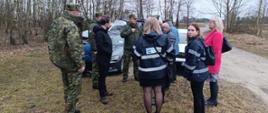 Wizja terenowa na odcinku przygranicznym z Białorusią. Przedstawiciele służb podczas wizji terenowej. Grupa kilkunastu osób stoi przy dwóch samochodach.