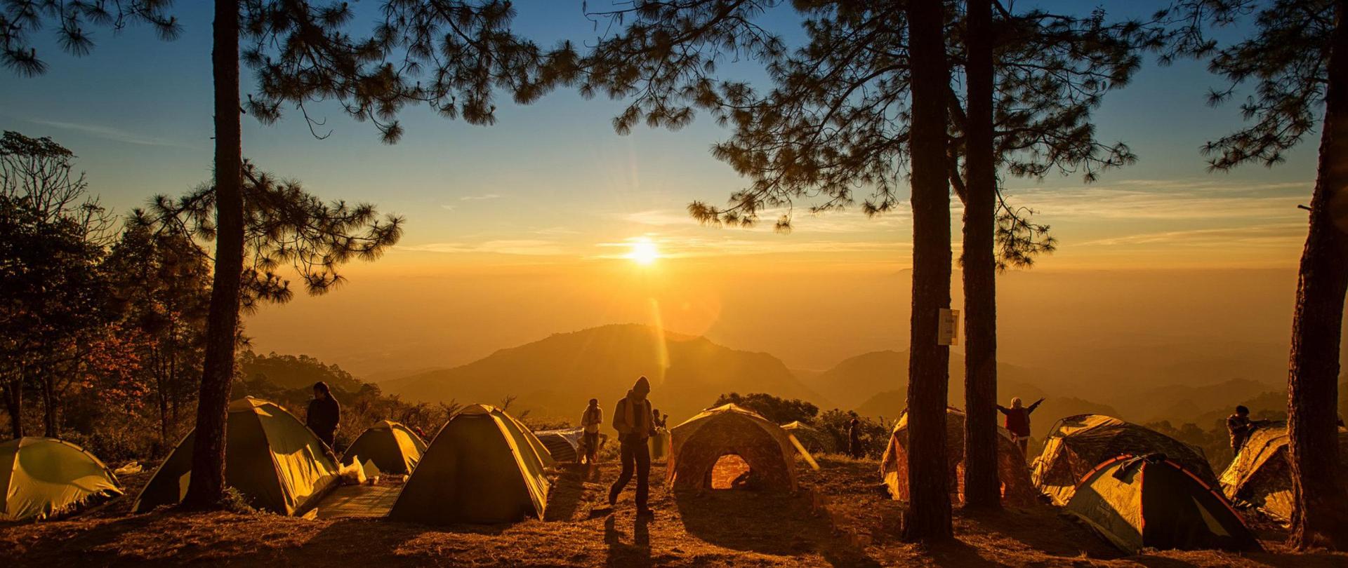 Namioty na górze, w tle zachodzące słońce.