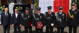 Pamiątkowe zdjęcie na tle sceny z banerem jubileeuszowym „Jubileusz 70-lecia Ochotniczej Straży Pożarnej w Bujałach Mikoszach”.
Przedstawia odznaczonych druhów oraz przedstawicieli władz i PSP trzymających dyplomy, legitymacje oraz medale.
Po lewej stronie na scenie widoczna jest spikerka prowadząca uroczystość przy mównicy.